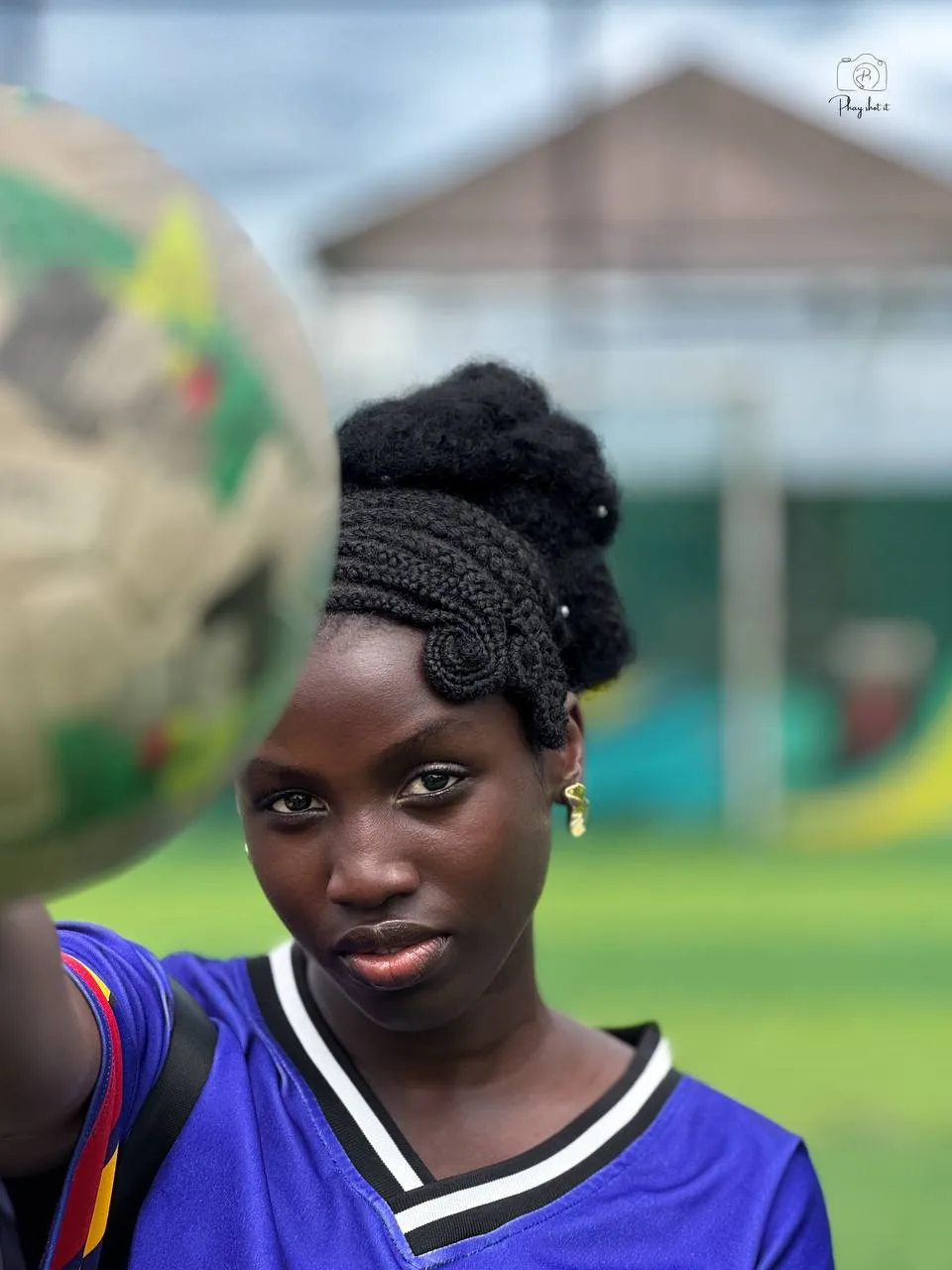 Young woman with braided updo holding a football, close-up portrait with intense gaze.