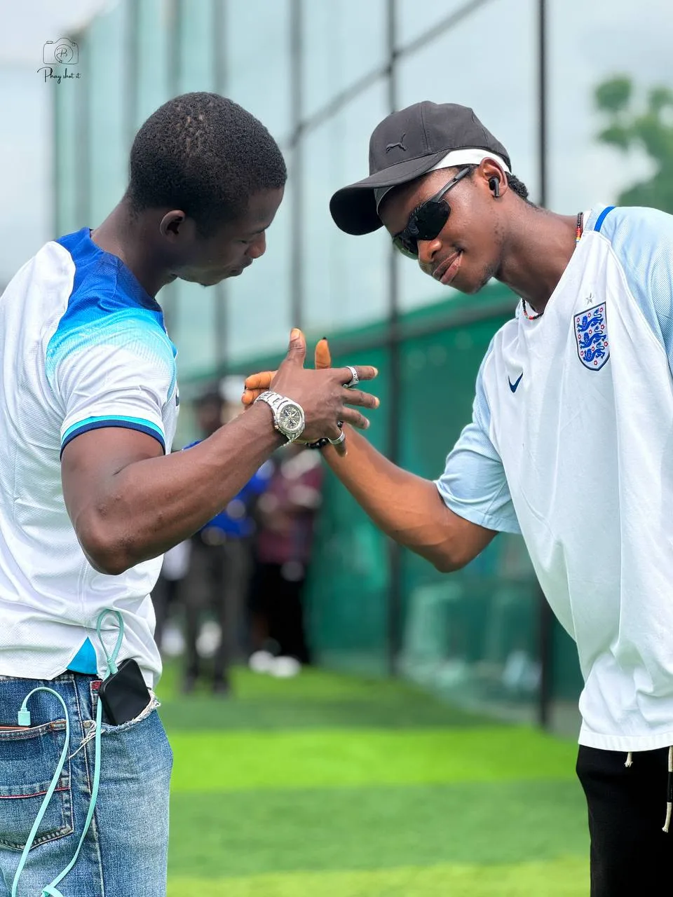 Two men greeting each other on a football pitch, one in England jersey, captured mid-handshake.