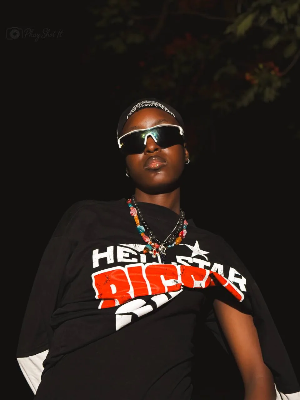 Woman with bandana and sunglasses in dark interior, moody close-up portrait.