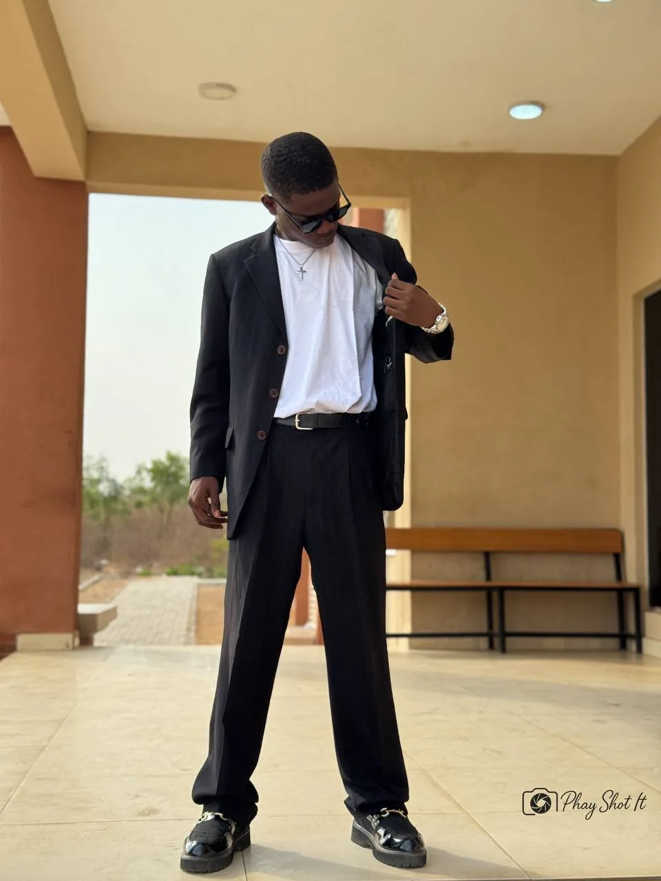 Man in black suit jacket and white t-shirt looking down, fashion portrait in architectural setting.