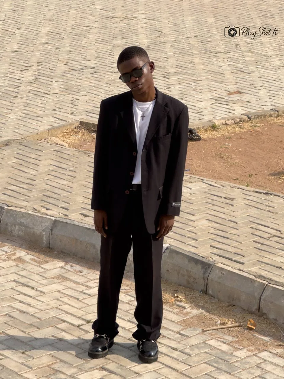 Man in dark suit on cobblestone pavement, full-length fashion portrait.